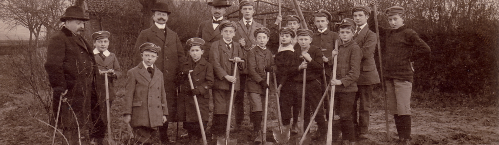 Jüdische Schüler bei der Gartenarbeit mit Gartenwerkzeug vor einem Haus und Bäumen in schwarz-weißer Abbildung.